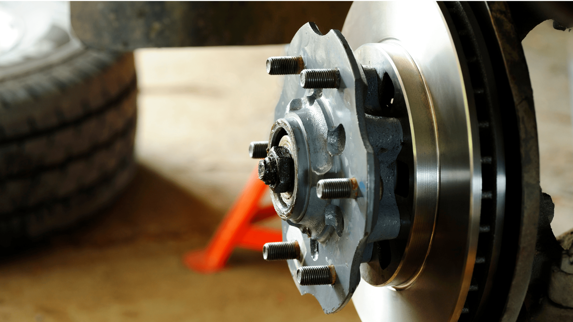 Car wheel hub with exposed brake rotor and lug bolts in a garage, tire in background