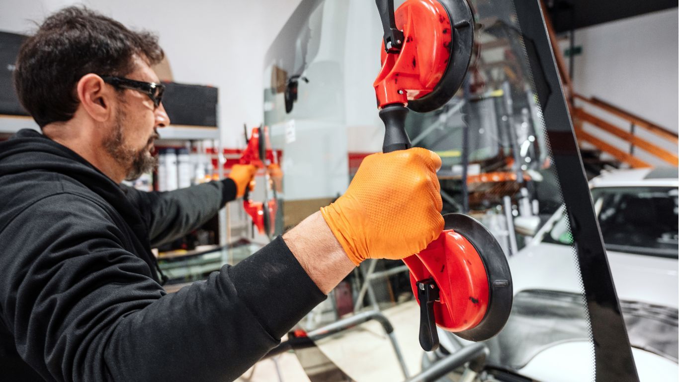 Technician wearing gloves uses a suction tool to install or repair glass on a vehicle