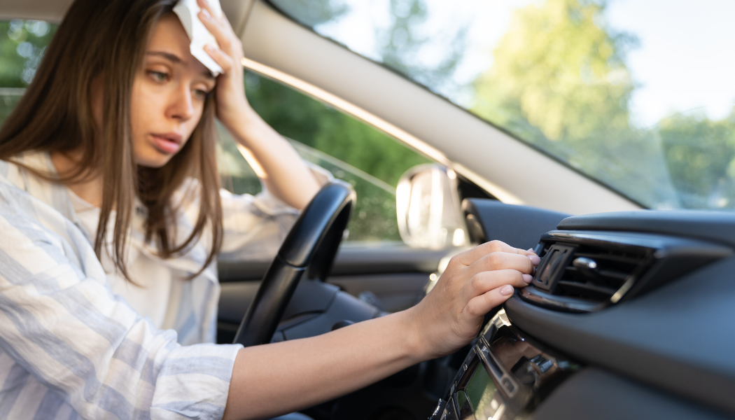 Woman in a car, looking stressed and holding her forehead while reaching toward the dashboard.