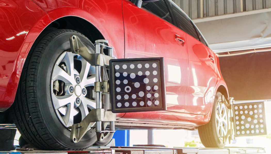 Red car on wheel alignment rack in an auto repair shop, with alignment equipment beside the front wheel