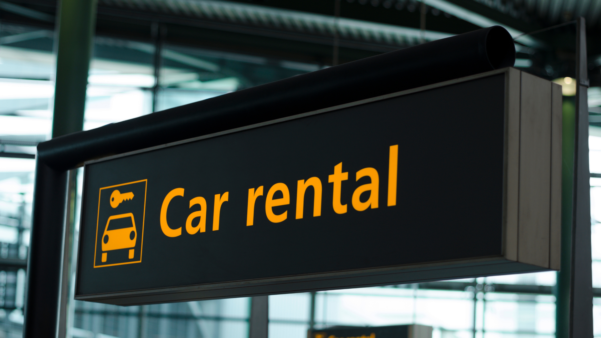 Car rental sign with orange text and car icon on a black airport-style display