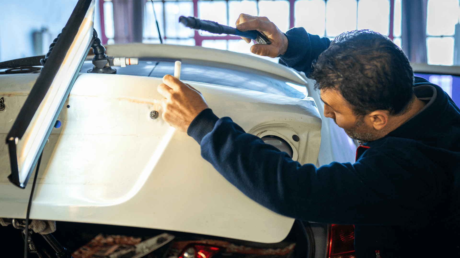 Person inspecting the inside of a car door with tools in a garage