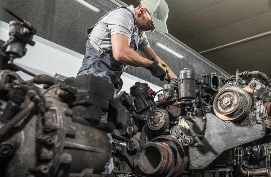 Mechanic inspecting engine components in a workshop surrounded by dismantled machinery