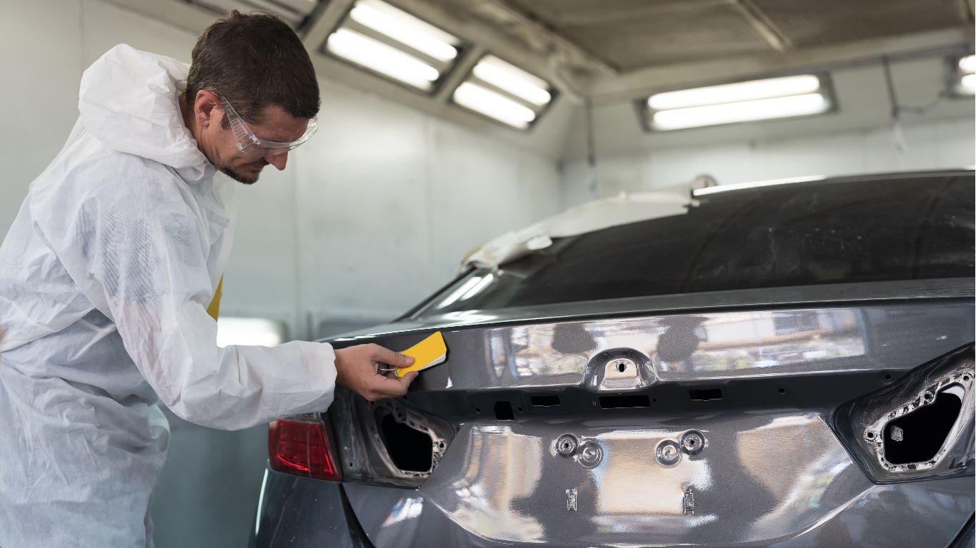 Technician sanding the rear of a silver car in a auto body shop