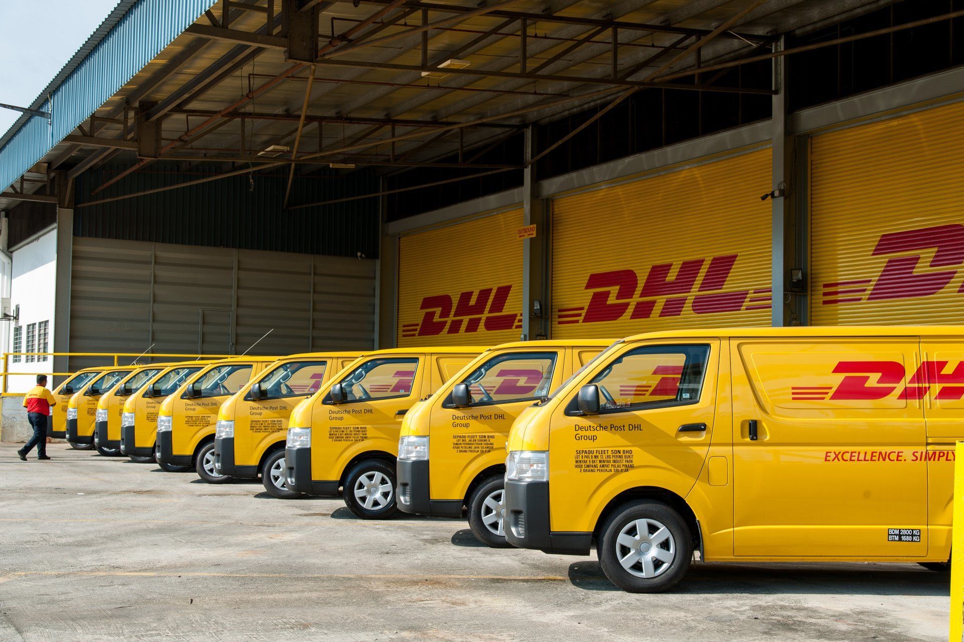 Row of yellow DHL delivery vans parked in a warehouse loading area