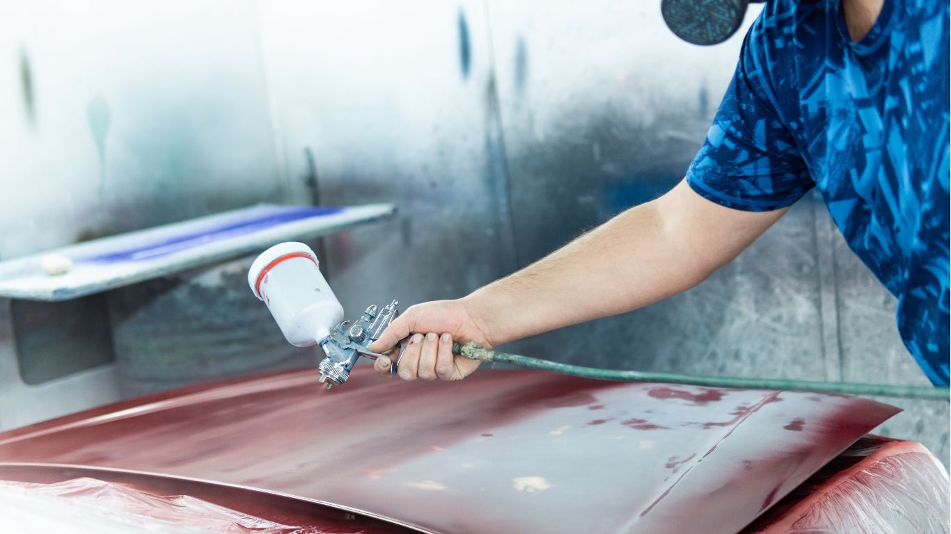 Person spray-painting a red car hood in a paint booth