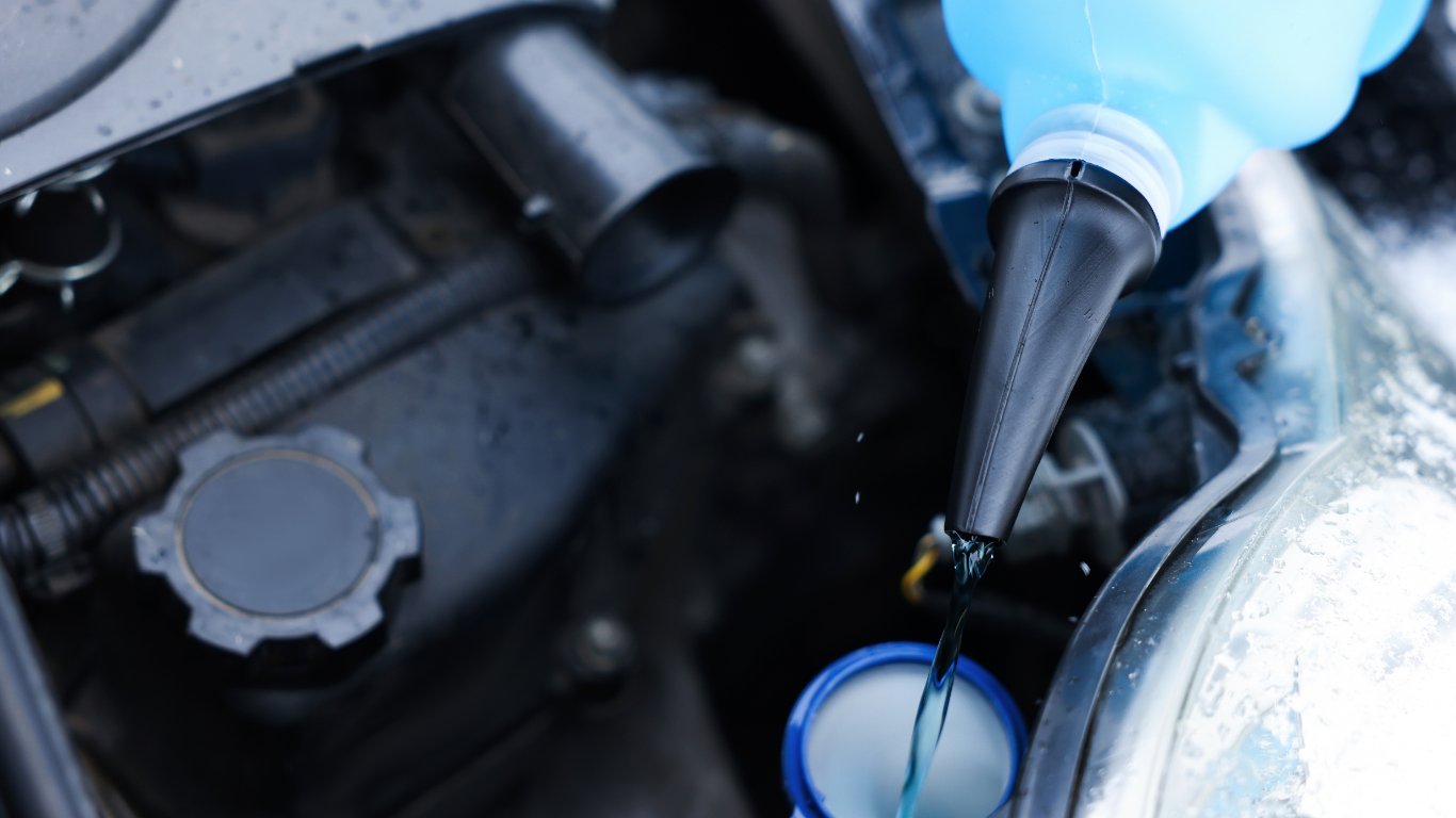 Blue-gloved hand adding fluid to a car engine reservoir with a black funnel