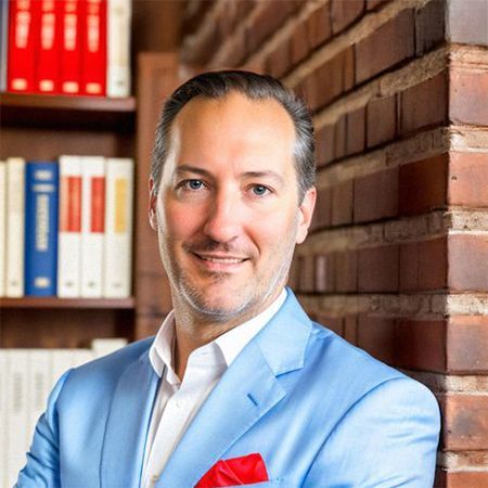 A man in a blue suit is leaning against a brick wall. Dr. Steve Ward