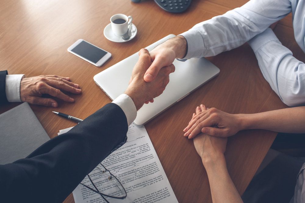 Two People Shaking Hands Over a Table, Symbolising Agreement or Deal — Country Coast Valuers in Laurieton, NSW