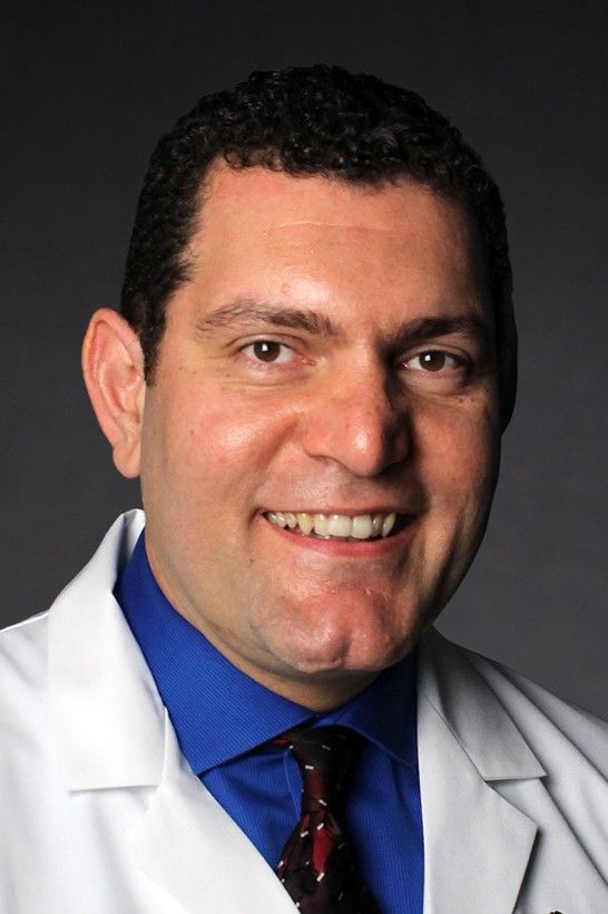 A smiling man wearing a white coat and tie