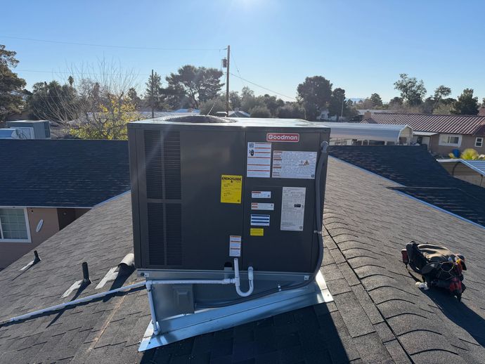 Roof-mounted HVAC unit on a shingled rooftop under a clear sky, with warning labels visible