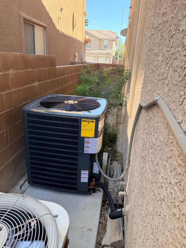 Outdoor HVAC condenser units in a narrow side yard beside stucco walls and a brick fence