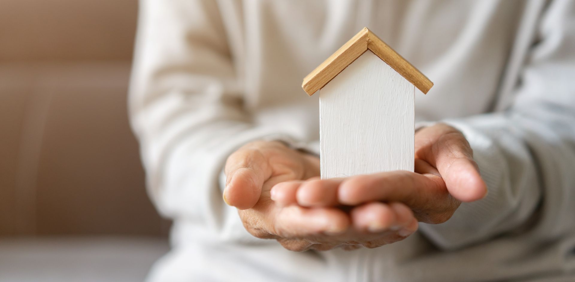 Hands holding a small white house model with a tan roof