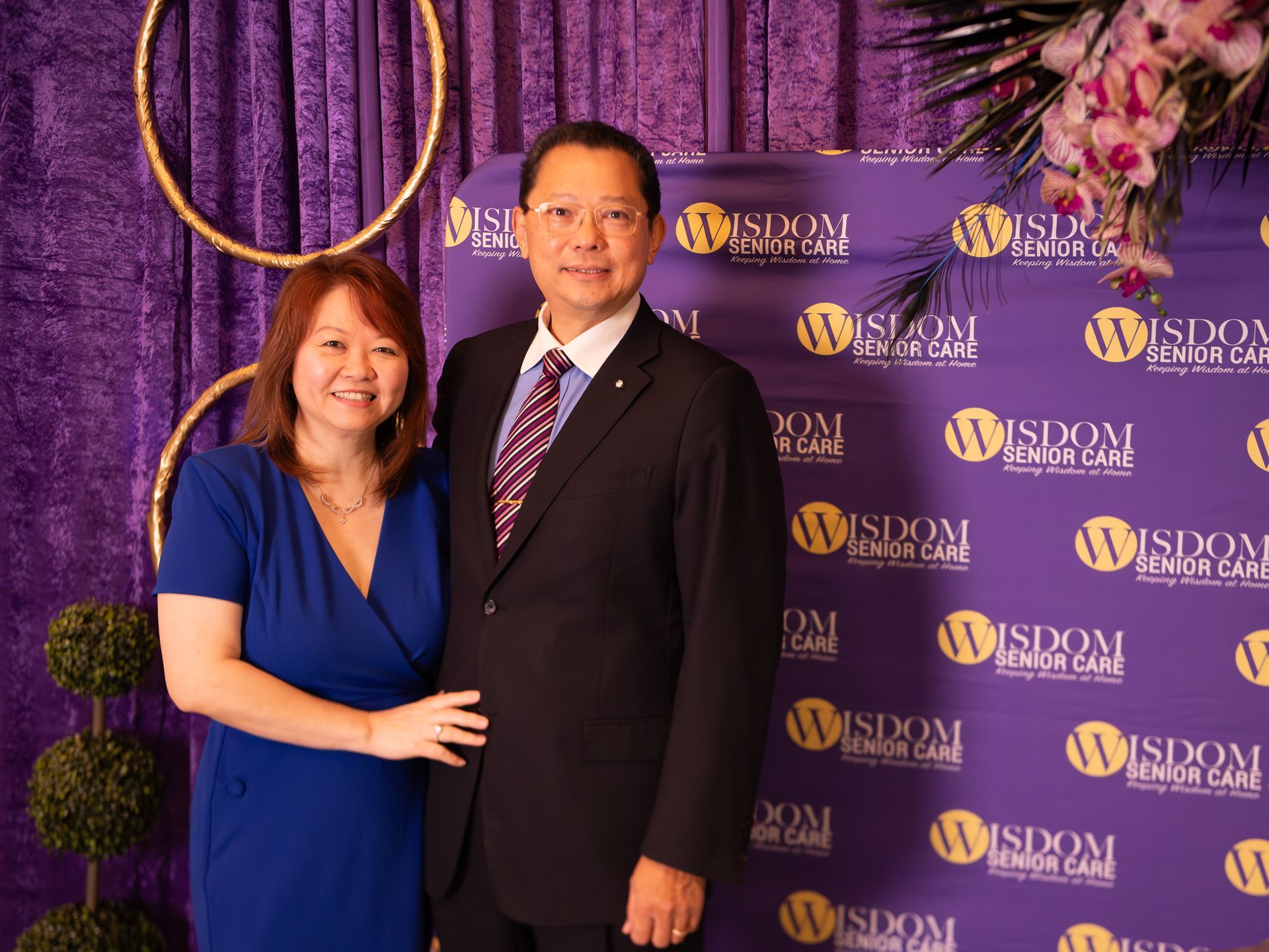 Two people posing at a WISDM event backdrop, with a woman in a blue dress and a man in a dark suit.