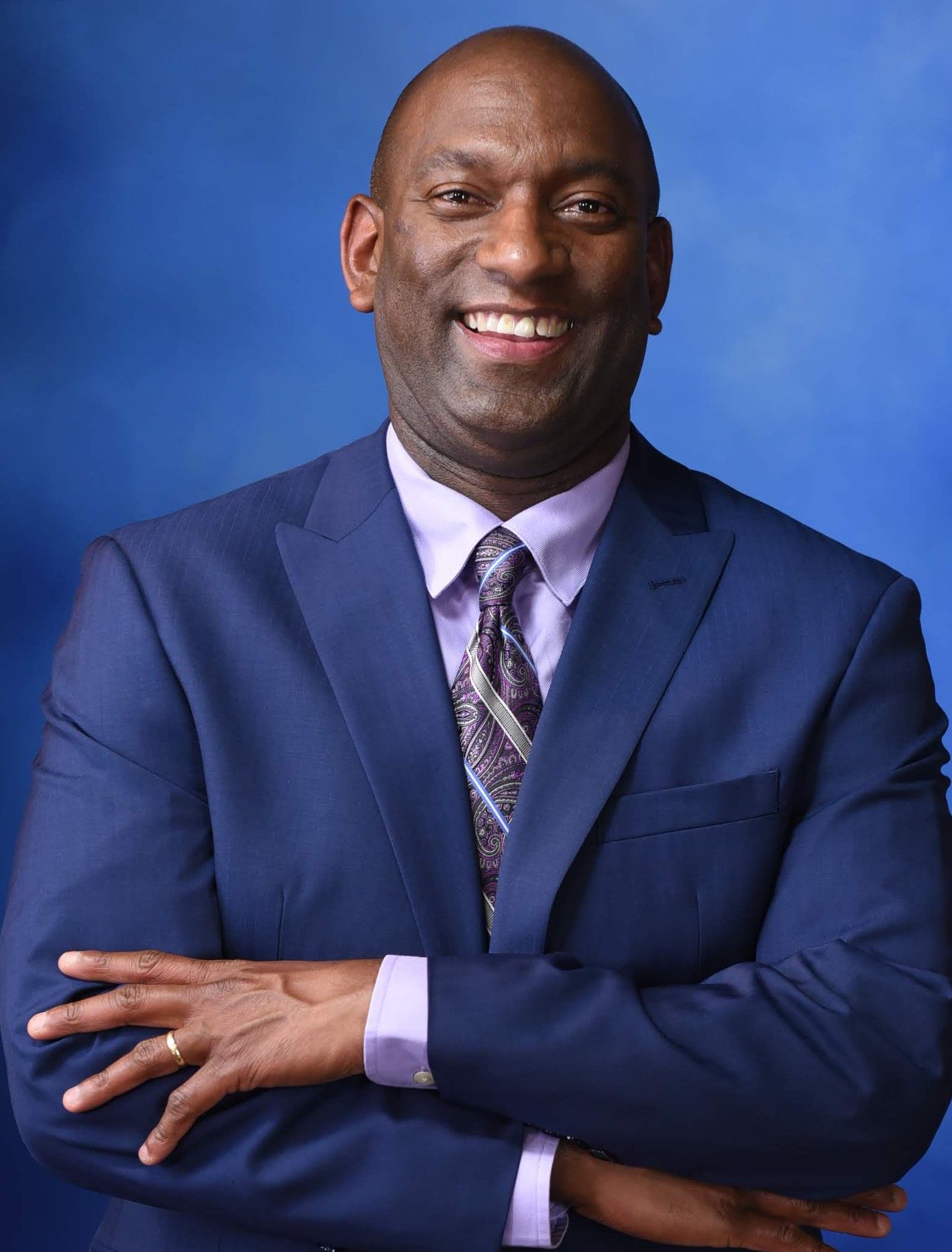Smiling man in a blue suit with arms crossed against a blue background