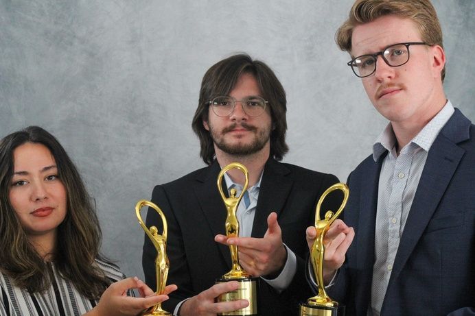Three people holding golden awards, standing in front of a gray backdrop.