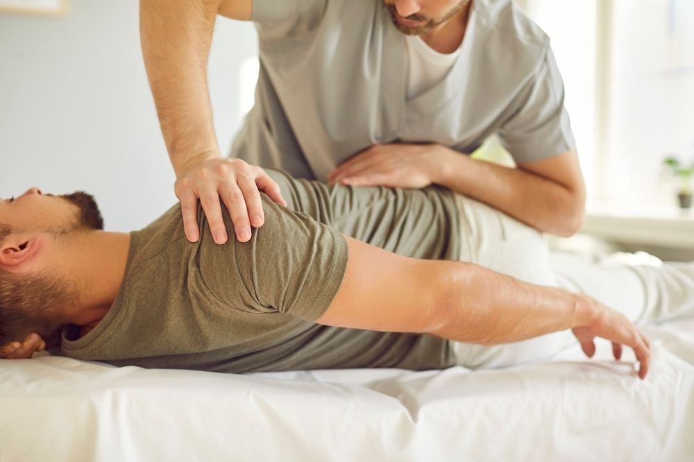 Physical therapist guiding a patient through a back stretch on a treatment table