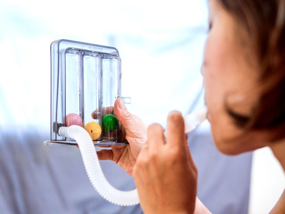 Person using an inhaler attached to a clear chamber with medication capsules inside.