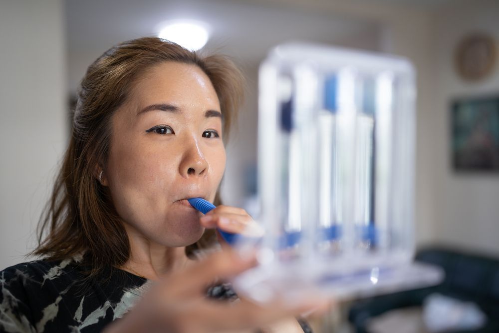 Woman blowing into a blue test tube in a lab or medical setting, with a clear cup in the foreground