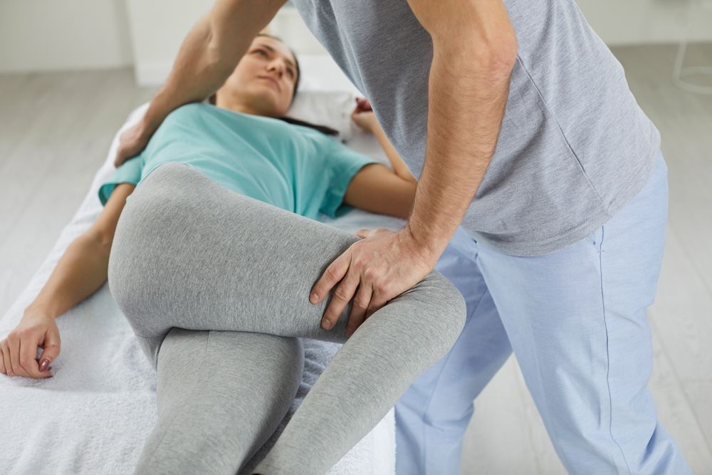 Physical therapist assisting a patient doing a leg stretch on a treatment table