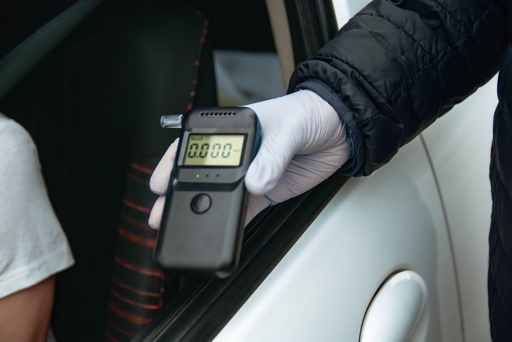 Handheld breathalyzer testing device held by a gloved hand near a car door