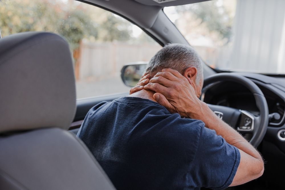 Man sitting in a car, holding his head with both hands, appearing stressed or in pain