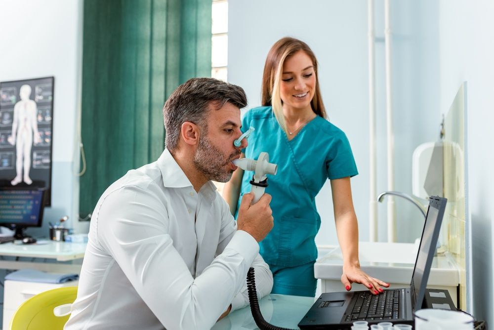 Clinician demonstrating a breathing device to a patient at a laptop in a medical office