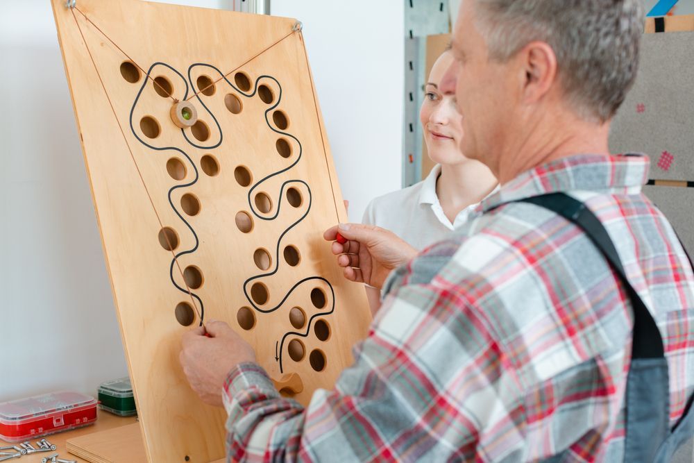 Two people playing a wooden peg-and-hole game, moving pieces on a board indoors