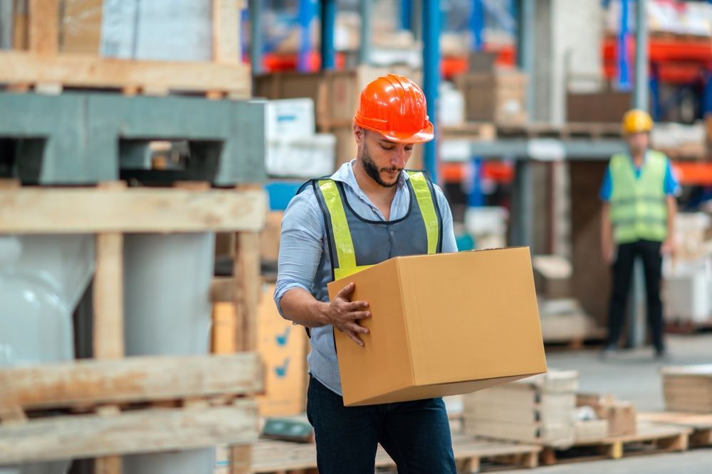 Construction worker in orange hard hat carrying a cardboard box at a building site