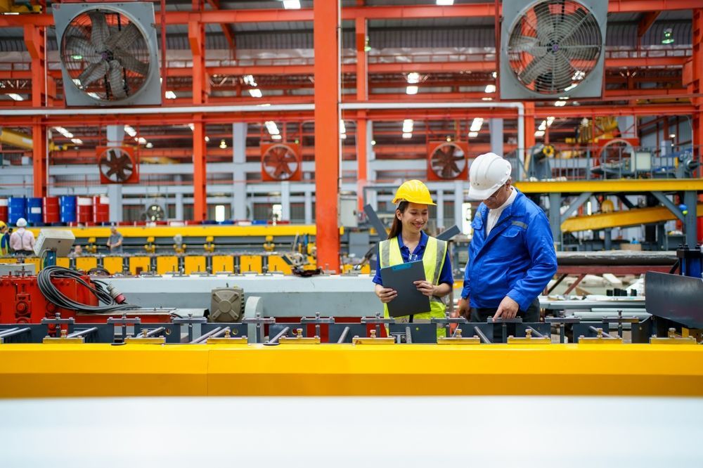 Two workers in hard hats inspect machinery in a bright industrial factory.