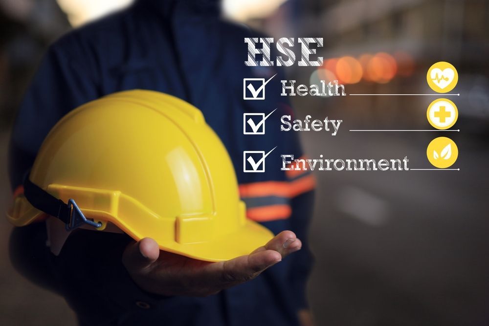 Yellow hard hat in a hand with “HSE” checklist icons for health, safety, and environment.