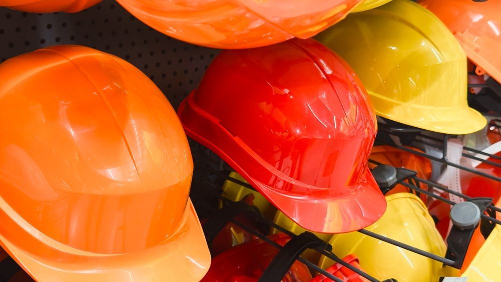 Orange, red, and yellow hard hats stacked together on a wire rack.