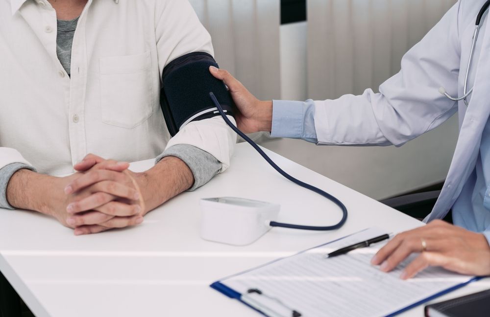 Healthcare worker checking blood pressure on a seated patient’s arm at a desk
