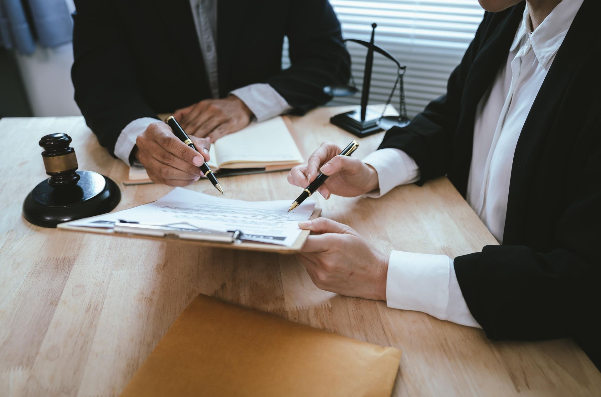 Three people in business attire signing documents at a conference table with a stamp and papers.