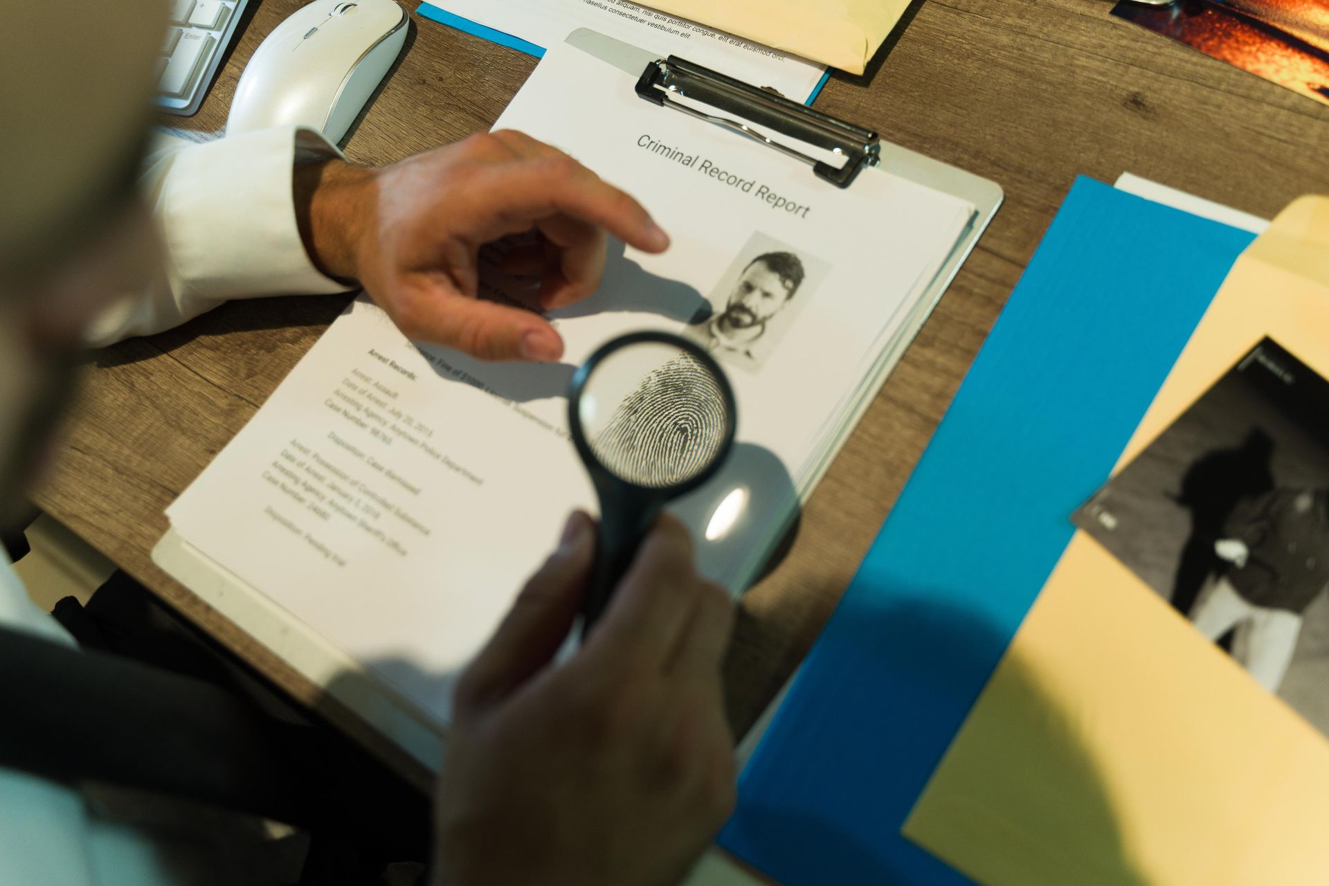 Hands using a magnifying glass to examine a document on a desk with papers and folders