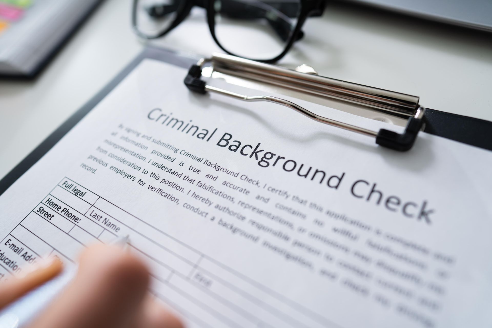 Criminal background check form on clipboard with eyeglasses and hand nearby
