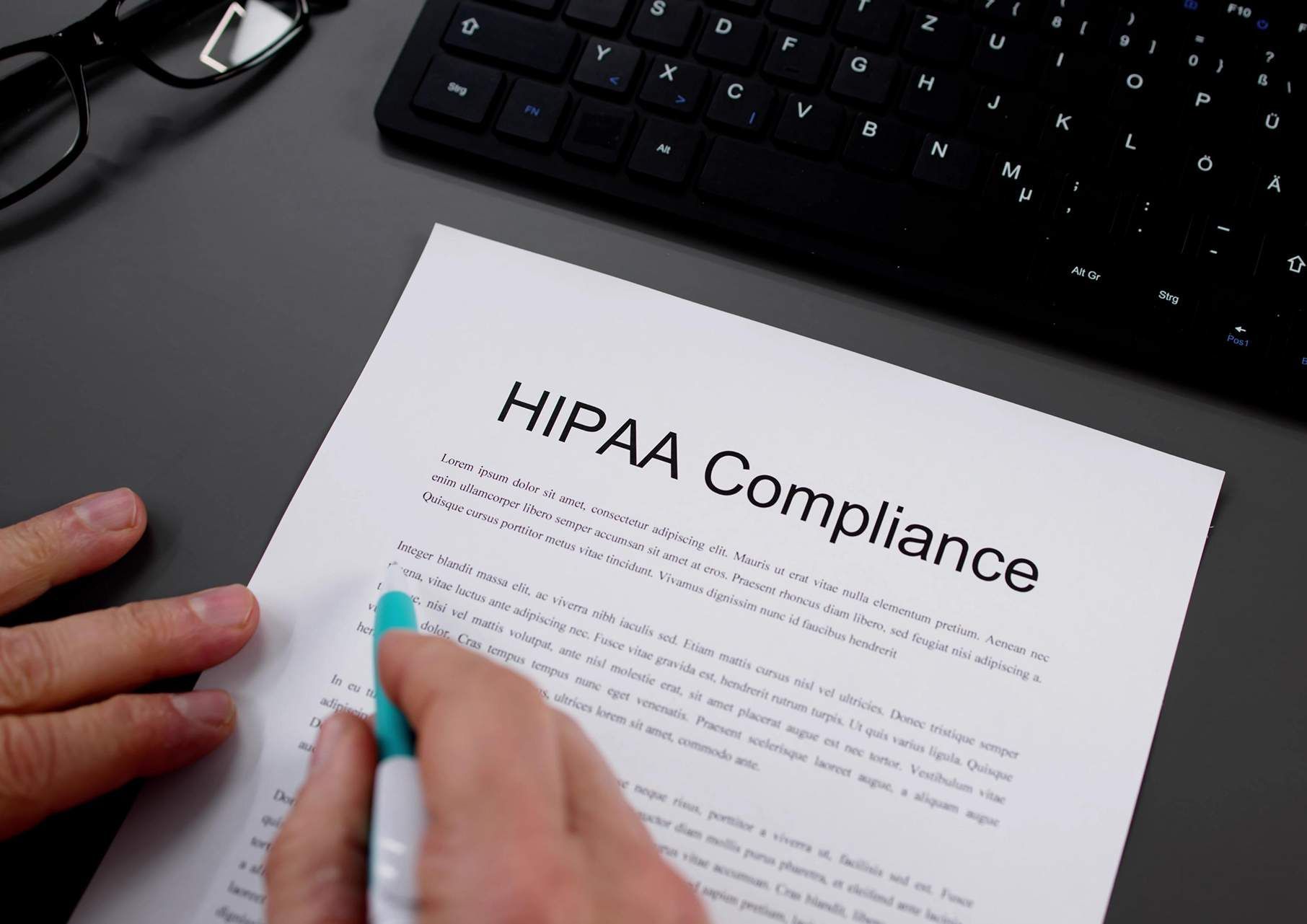 Hands reviewing a HIPAA Compliance document beside a keyboard on a desk.