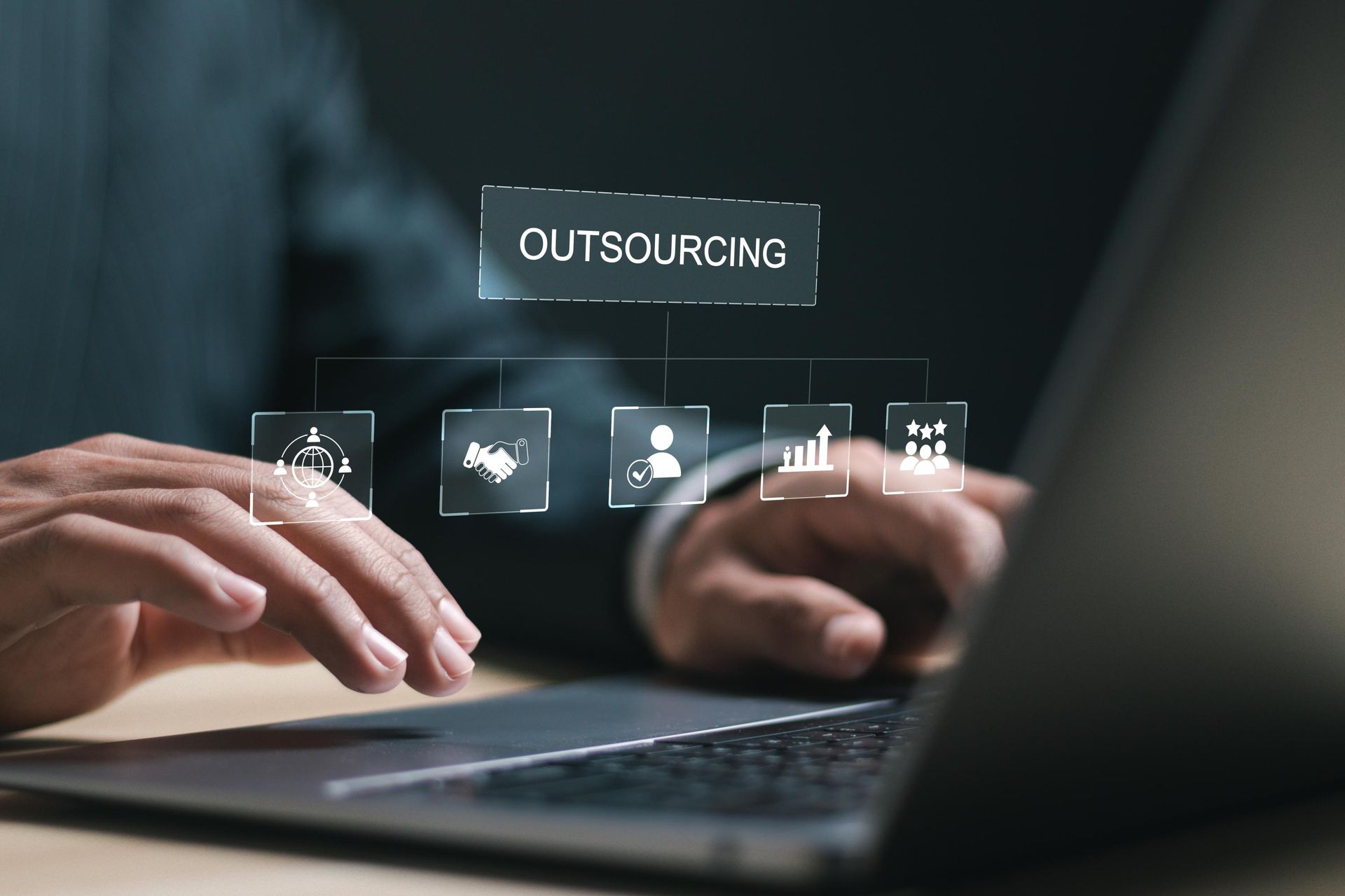 Hands typing on a laptop with a digital “OUTSOURCING” interface floating above the keyboard