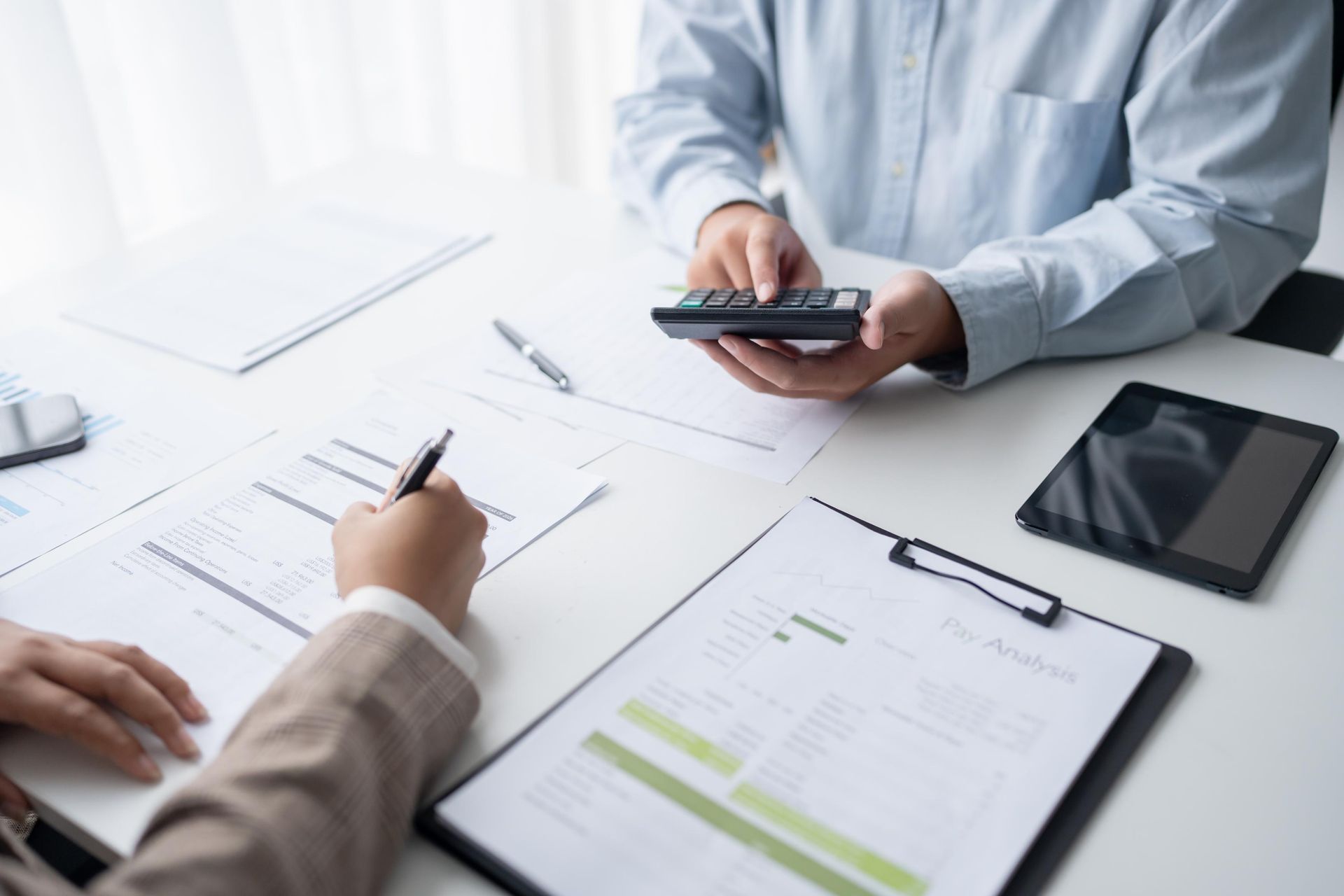 People reviewing financial documents at a desk with a calculator, tablet, and pen