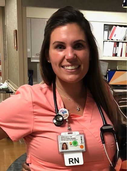 Smiling nurse in pink scrubs with stethoscope and ID badge standing in a hospital hallway