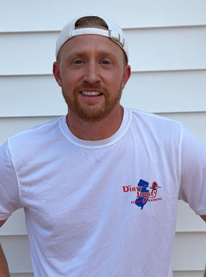 Smiling man in white shirt and backward cap standing outdoors against white siding