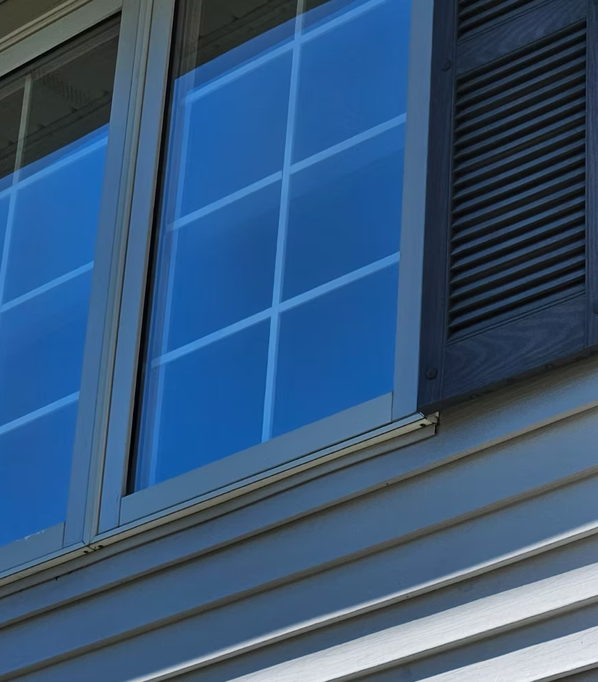Blue house window with white trim and black shutters on light gray siding