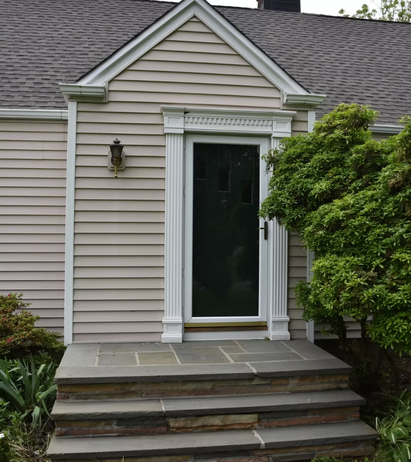 Front steps leading to a white-trimmed front door beside a green shrub on a beige house