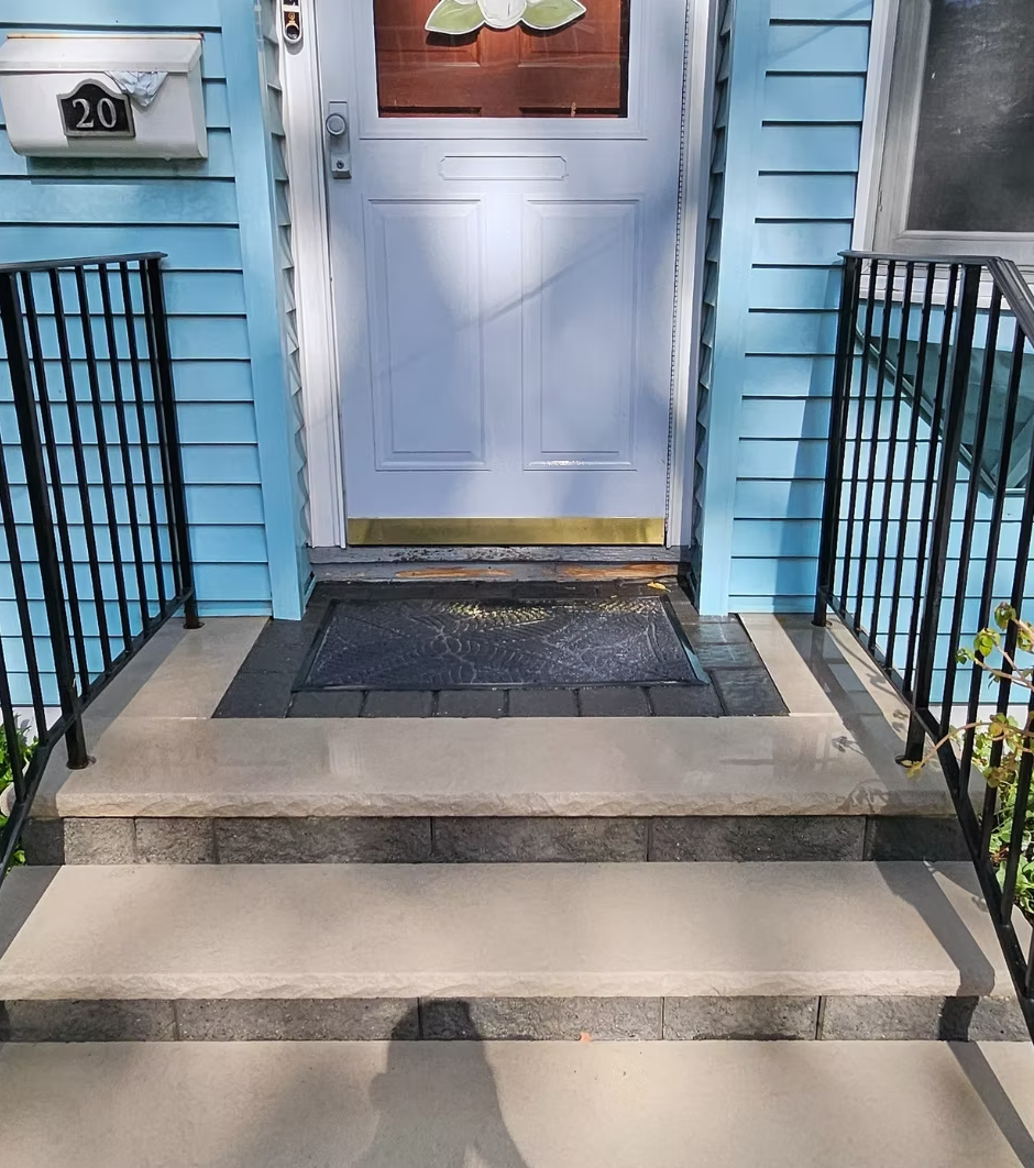 Front steps to a light blue house with a white door and black railings, house number 20 visible