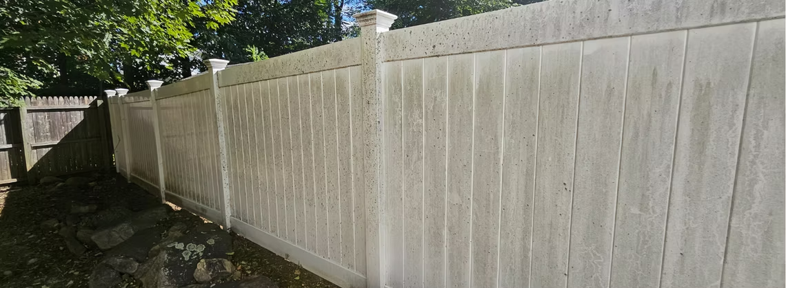 Tall white wooden fence along a leafy backyard path in daylight
