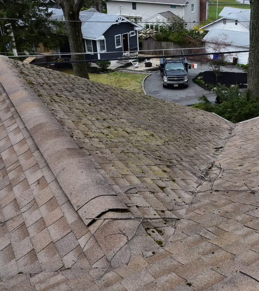 Weathered shingle roof with damaged ridge, overlooking a driveway and houses below