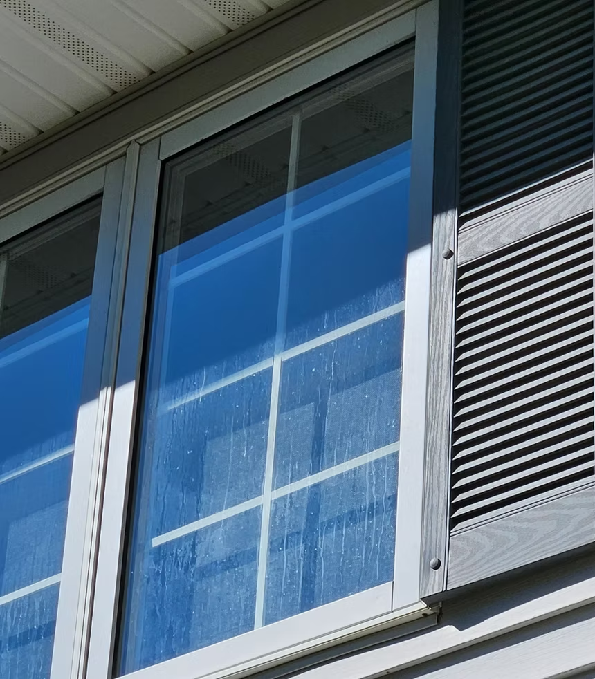 Close-up of a blue house window with white trim and dark shutters reflected in the glass