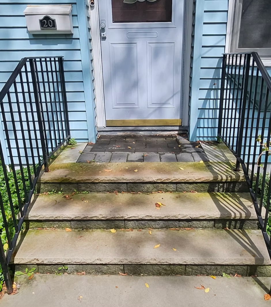 Front steps with black railings leading to a white front door on a light blue house.