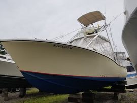 Large white-and-blue fishing boat on a trailer in a yard, viewed from the bow.