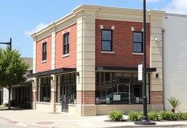 Corner brick storefront with red facade, large windows, and beige trim on a sunny street corner.